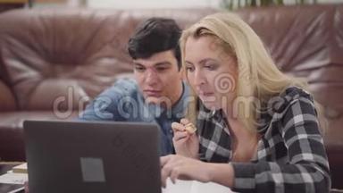 一对年轻夫妇坐在家里的笔记本电脑前。一个黑发男人和一个金发女人一起在笔记本电脑前工作的肖像